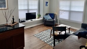 Una sala de estar moderna con un televisor de pantalla plana, un sillón cómodo, una mesa de centro y una mesa de comedor.