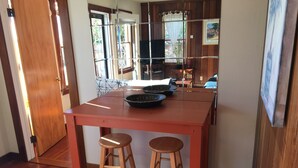 Cuina amb taula de fusta, dos tamborets, un televisor i una finestra amb cortines.