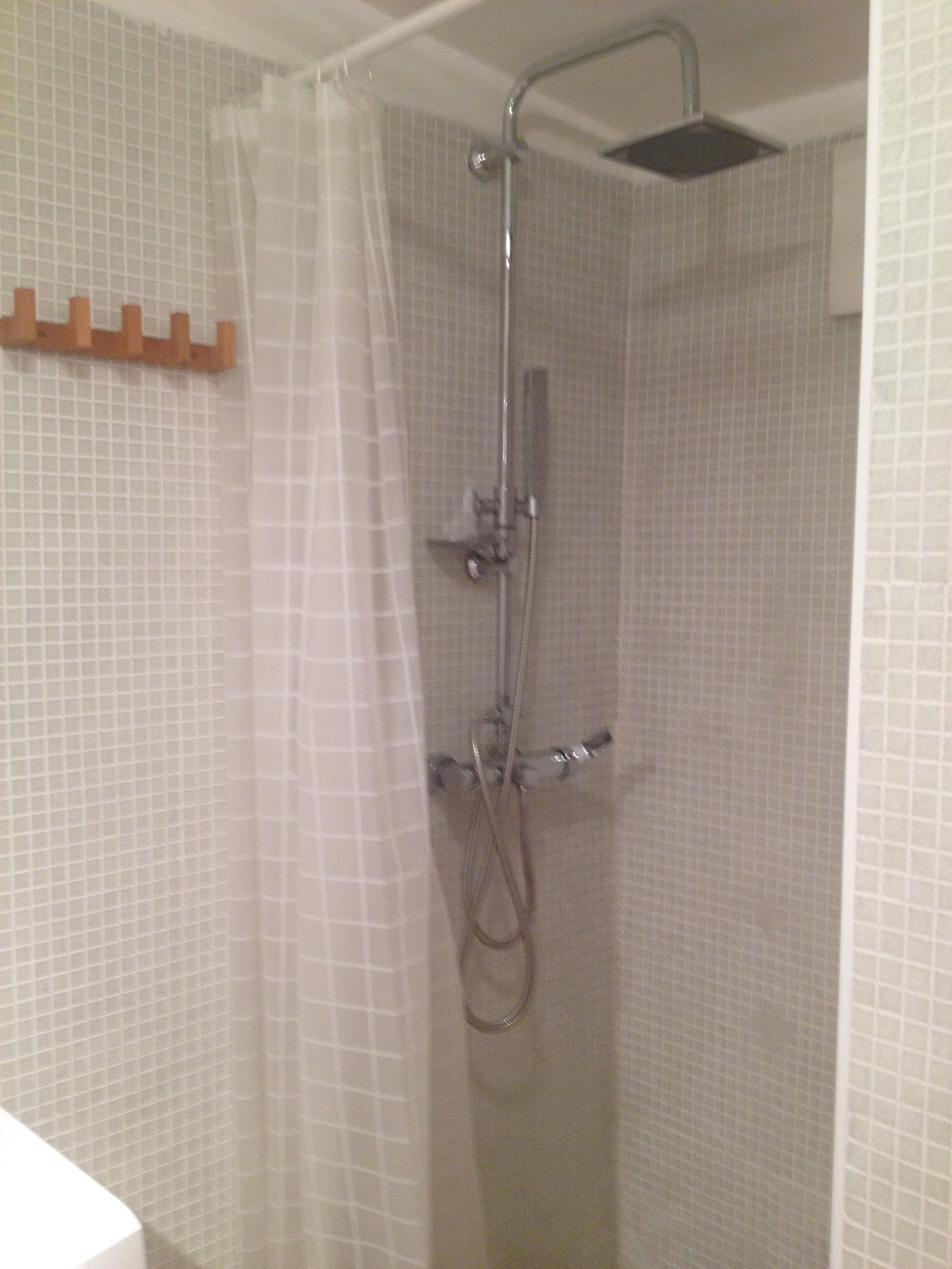 Ducha con mampara de vidrio, cabezal de ducha de mano y grifo empotrado en la pared.