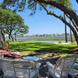 A patio area with wicker chairs and a small table, overlooking a body of water and a marina with boats.