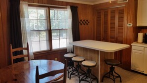 A small kitchen with a wooden table and stools, a window with blinds, and a white cabinet. - Breathtaking Waterway Views. 1BR. 1Bath. Kitchen. Porch. 2 Person. 5 Star Views (Ocean Isle Beach)