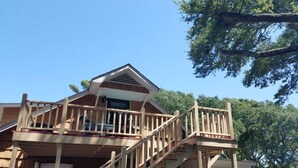A wooden cabin with a balcony, a staircase, and a red door. - Breathtaking Waterway Views. 1BR. 1Bath. Kitchen. Porch. 2 Person. 5 Star Views (Ocean Isle Beach)