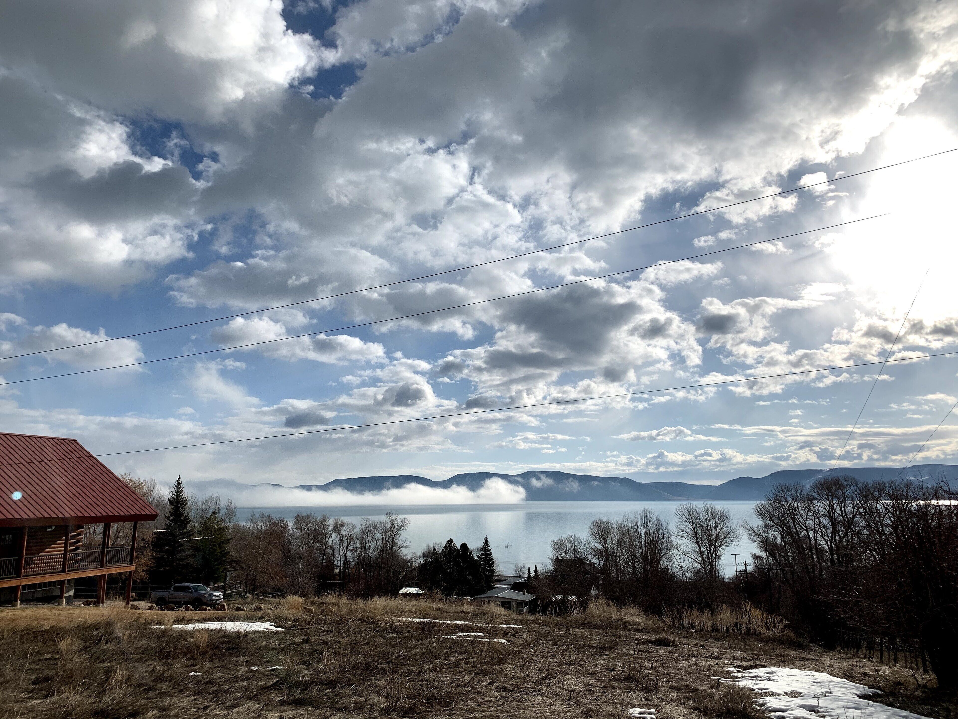 A cabin with a red roof, a view of a lake, and mountains in the distance.