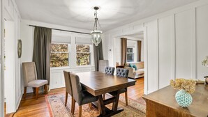 A dining area with a wooden table and chairs, a chandelier, and a view through large windows. - Fun Rec room, Hot Tub & Mountain View’s 2 King Rooms (Candler)