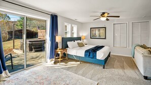 A bedroom with a bed, a ceiling fan, a window with curtains, a nightstand, and a view of the outdoors. - Fun Rec room, Hot Tub & Mountain View’s 2 King Rooms (Candler)