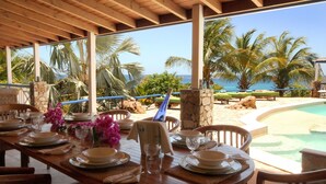 A dining area with a view of the ocean, equipped with tables set for dining, chairs, and a pool in the background. - The Carib House, Turtle Bay 5 room villa, pool, views, beach, English Harbour no (St Paul)