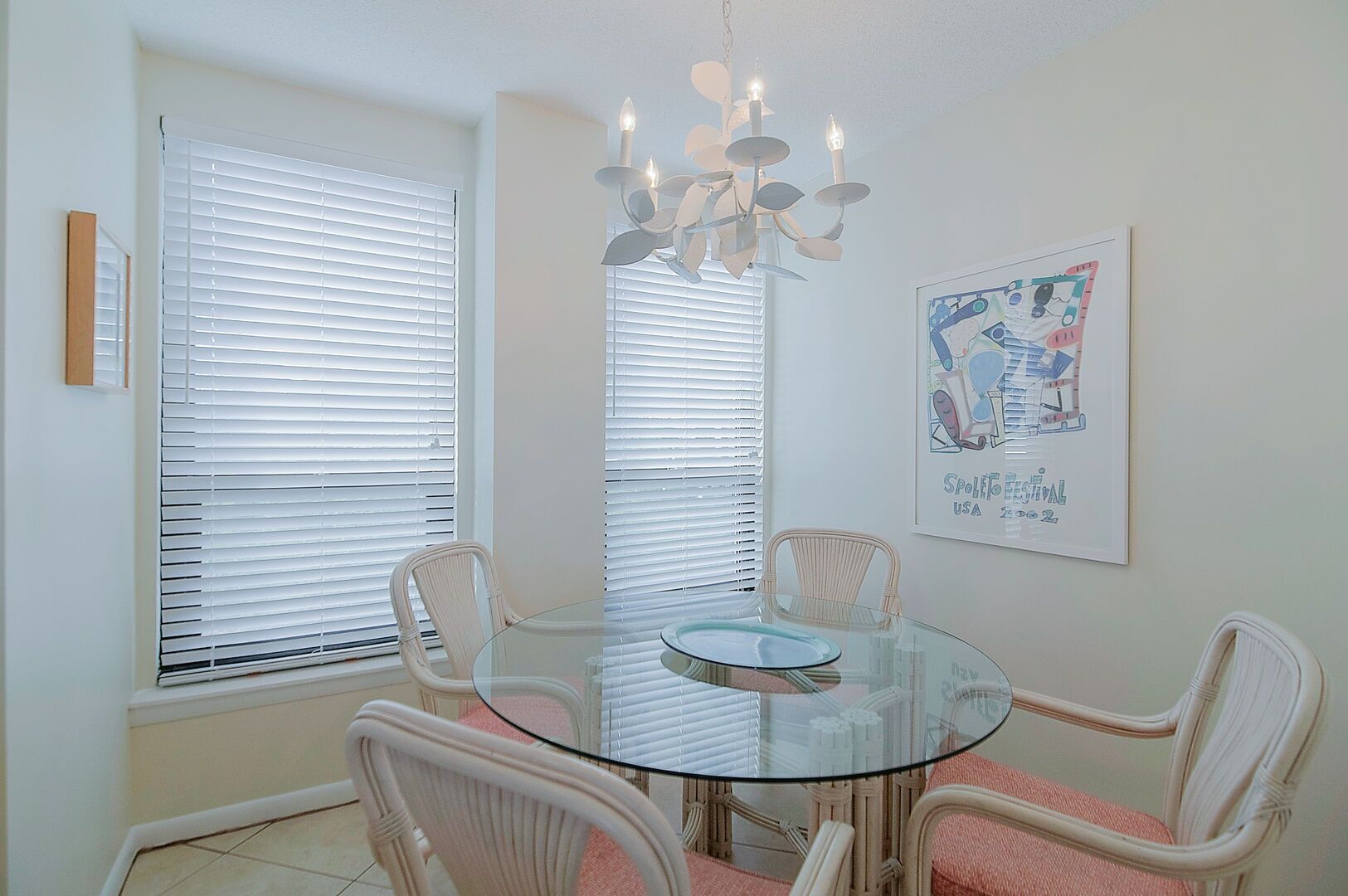 A dining area with a glass table surrounded by wicker chairs, white walls, and a chandelier.