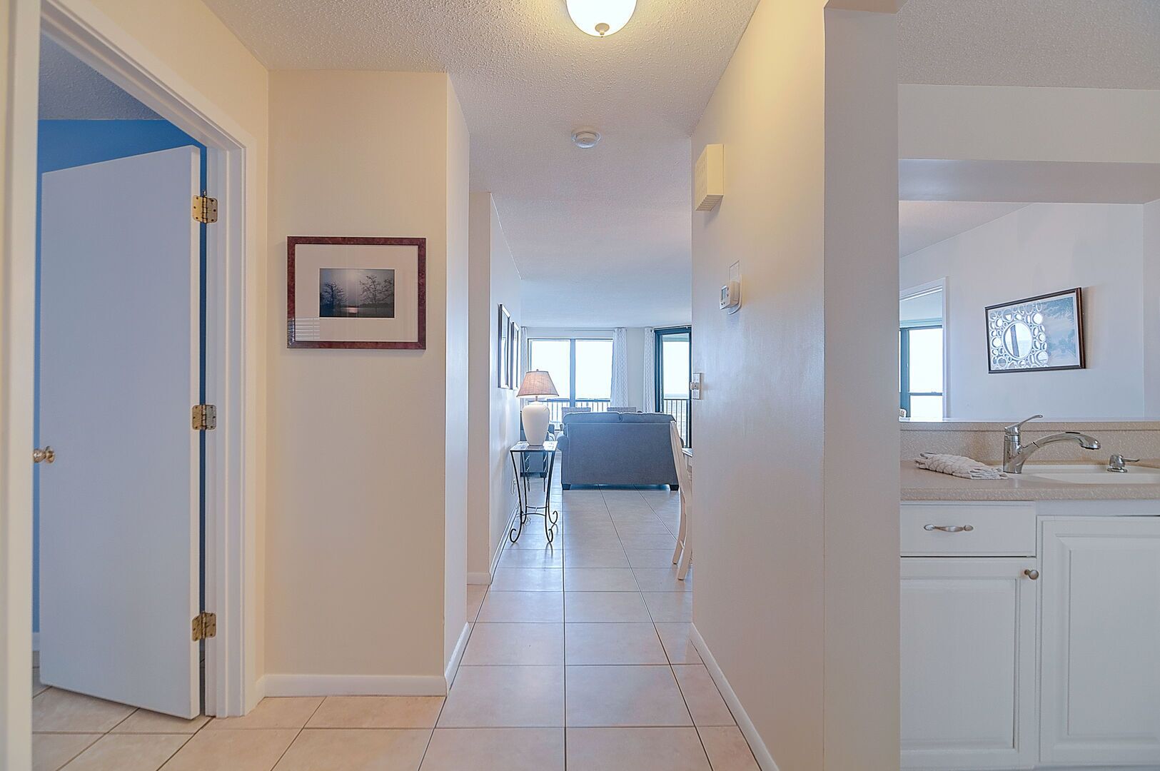 A hallway with a white door, a framed picture on the wall, and a kitchen area with a sink and cabinets.