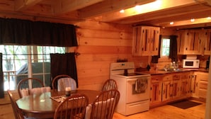 A wooden cabin interior with a dining table, chairs, a stove, and a kitchen area. - Cozy Authentic Amish Cabin, 5 Acres Of Privacy, 4 Wheel Trail, Snowmobile Trail (Lampson)