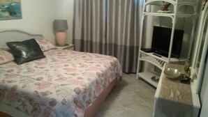 Ein Schlafzimmer mit Bett, Fernseher auf einem Schrank, Lampe und Regal mit Gegenständen.