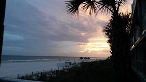 Ein Küstenblick mit Sonnenuntergang, Strand und einem Gebäude mit Zaun im Vordergrund.