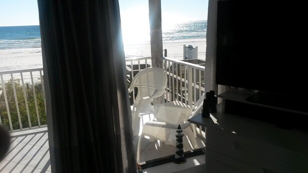 Ein Balkon mit weißem Stuhl und kleinem Tisch, mit Blick auf einen Strand, auf dem ein Schild mit der Aufschrift 'Nautical Watch' steht.