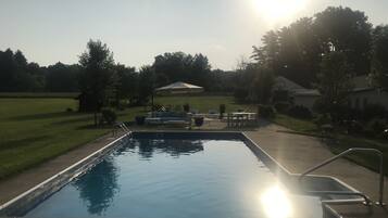 A swimming pool with a sunlit sky, grassy areas, and a gazebo.