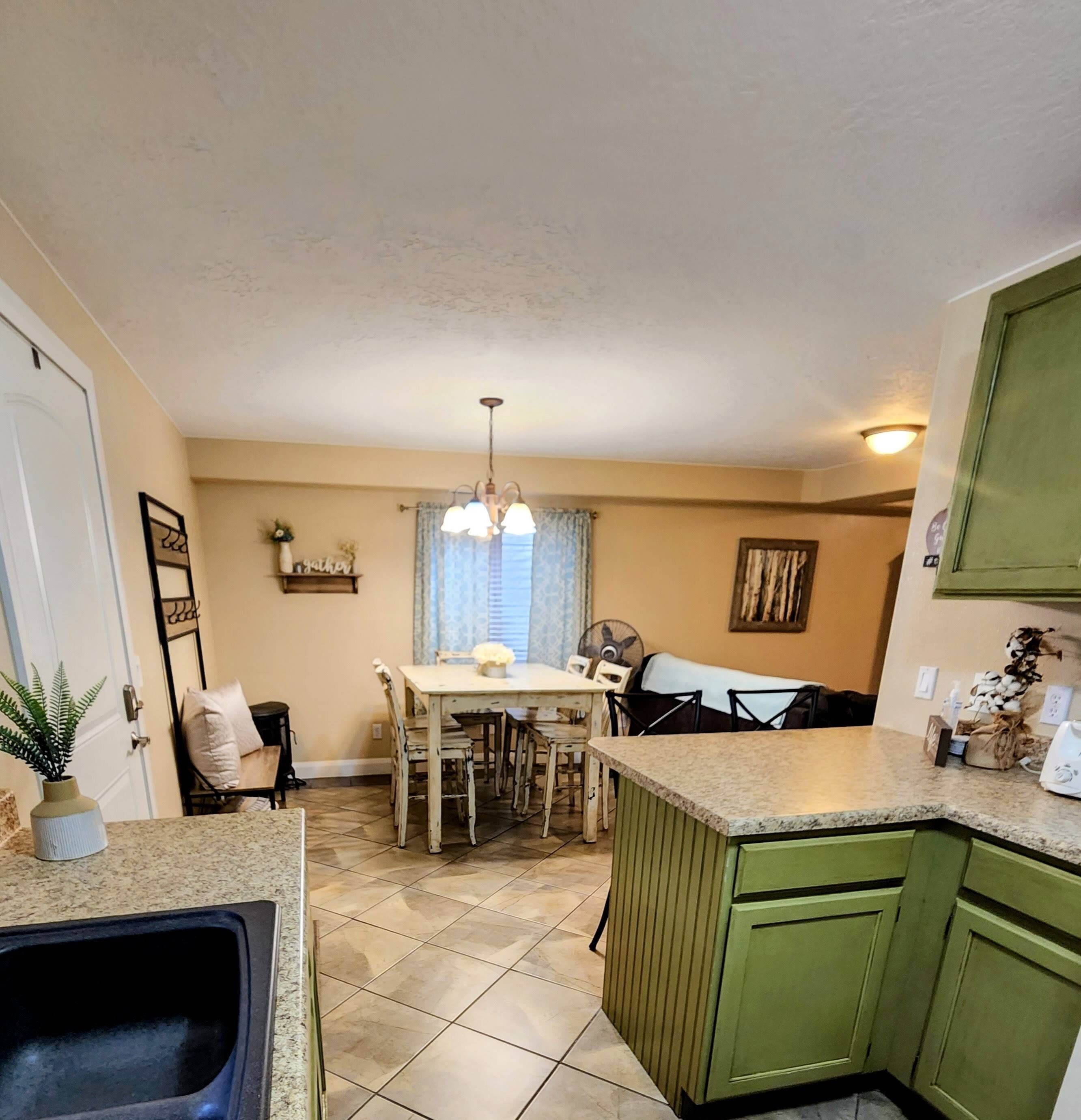 A kitchen with a dining table, chairs, a fan, and a green cabinet.