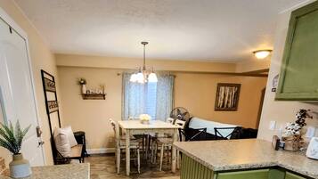 A kitchen with a dining table, chairs, a fan, and a green cabinet.