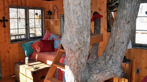 A cozy cabin interior with a loft bed, wooden walls, a large tree trunk, and a window with a view. - Rural appeal yet so close to town (Taos)