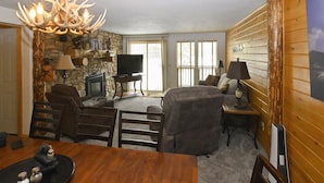 A cozy living room with a stone fireplace, a television, and a wooden dining table. - Yellowstone Rustic Luxury Condo Sleeps 11 in an Award Winning Resort (Island Park)