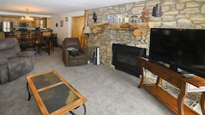 A living room with a stone fireplace, a television, and a dining area with wooden furniture. - Yellowstone Rustic Luxury Condo Sleeps 11 in an Award Winning Resort (Island Park)
