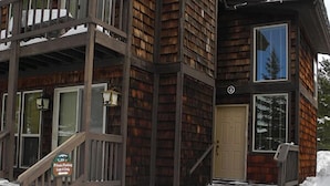 A wooden cabin with a wooden staircase leading to a front door, surrounded by snow. - Yellowstone Rustic Luxury Condo Sleeps 11 in an Award Winning Resort (Island Park)