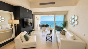 Een moderne woonkamer met een televisie, bank en een eethoek, die uitkomt op een balkon met uitzicht.