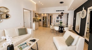 A modern living room with a white sofa, a coffee table, and a dining area with a round table and chairs.