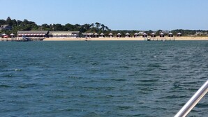 A beach with a row of beach huts and a pier extending into the water. - Charming Chappaquiddick Retreat: Steps from Private Beach & Edgartown's Best! (Edgartown)
