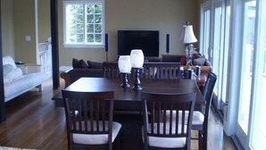 A dining area with a large wooden table, several chairs, a sofa, and a television in the background. - Charming Chappaquiddick Retreat: Steps from Private Beach & Edgartown's Best! (Edgartown)