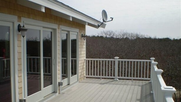 A deck with a white railing, a satellite dish, and a door with glass panels. - Charming Chappaquiddick Retreat: Steps from Private Beach & Edgartown's Best! (Edgartown)