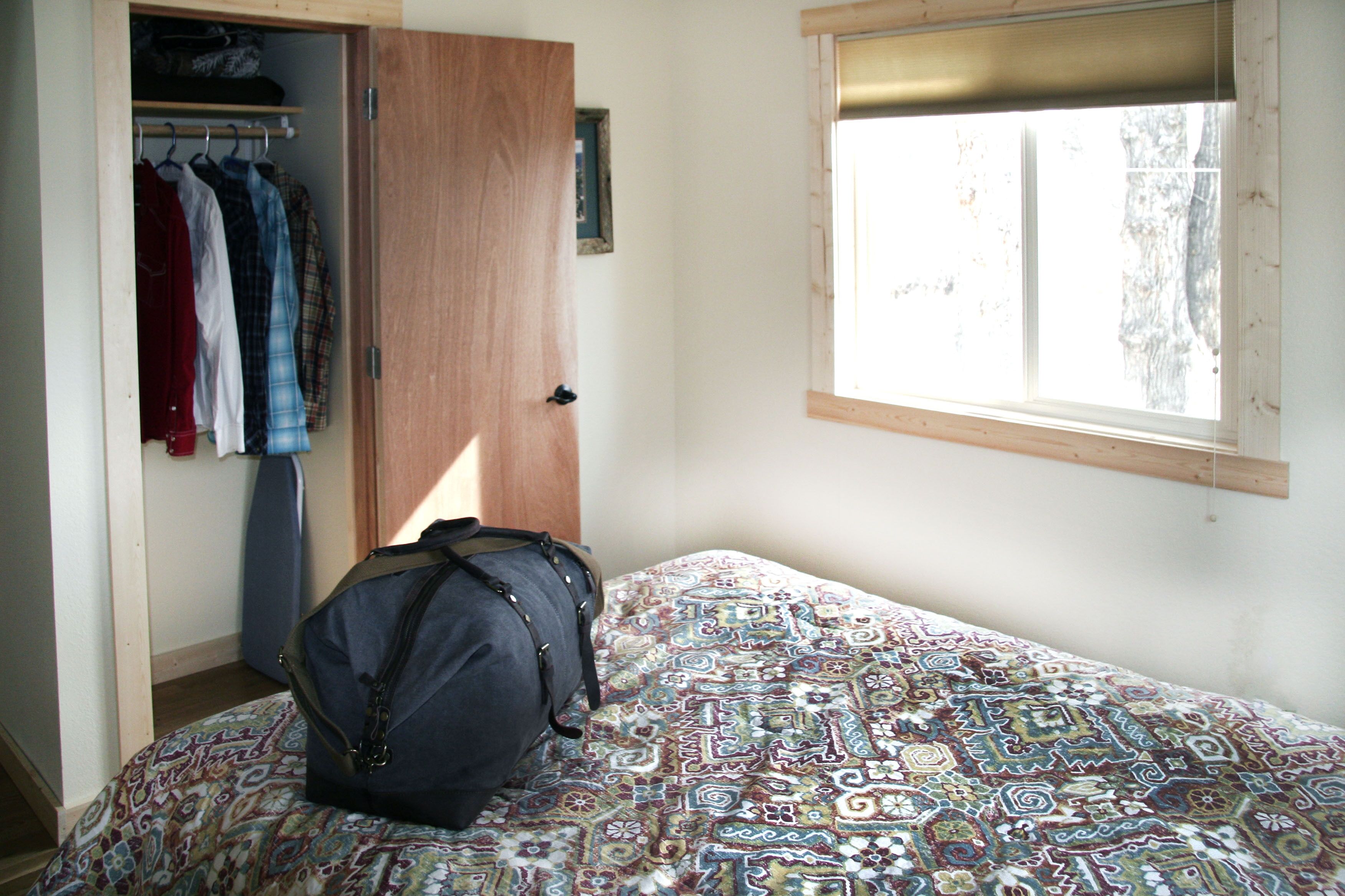 Una camera da letto con una coperta a motivi, un armadio pieno di abiti e una finestra con vista sugli alberi.