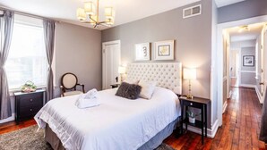 A hotel room with a large bed, a chandelier, a bedside table with a lamp, and a view of a hallway. - OTR Penthouse: Walk Everywhere & FREE Parking (Cincinnati)
