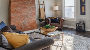 A living room with a brick wall, a leather armchair, a sofa, a coffee table, a lamp, and a record player. - OTR Penthouse: Walk Everywhere & FREE Parking (Cincinnati)