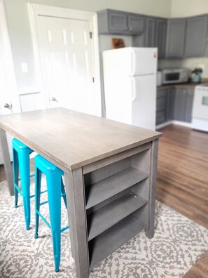 Una cocina con una mesa de madera clara, taburetes de bar color turquesa y armarios grises.