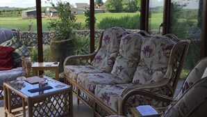 A conservatory with wicker furniture, a glass table, and a view of a green field and buildings. - Tullig Rock a Beautiful Country Home; Also available, Stone Cottage (Leap)