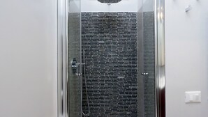 Una ducha con cerramiento de vidrio, pared con diseño de ladrillo y una pequeña ventana en la parte superior.
