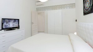 Un dormitorio con una cama, un televisor sobre una cómoda, un armario y una lámpara en el techo.