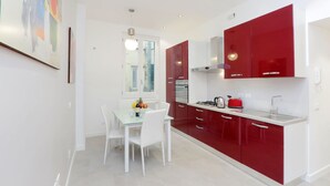Una cocina moderna con armarios blancos y rojos, una mesa de comedor de vidrio y una lámpara colgante.