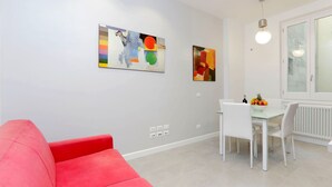 Una sala de estar moderna con un sofá rojo, una zona de comedor con una mesa de vidrio y dos cuadros abstractos en la pared.