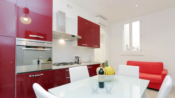 Una cocina moderna con armarios rojos, una mesa de comedor blanca y un sofá rojo.