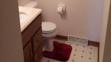A small bathroom with a toilet, sink, and a red rug on the floor.