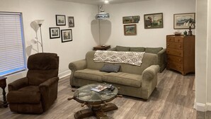 En stue med en brun lænestol, en beige sofa, et glasbord og en trækommode.