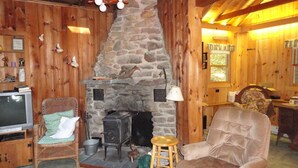 A cozy cabin interior with a stone fireplace, wooden walls, a television, and a comfortable seating area.
