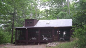 A cabin with a porch, large windows, and a chimney.