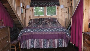 A wooden cabin bedroom with a bed, dresser, and a staircase.