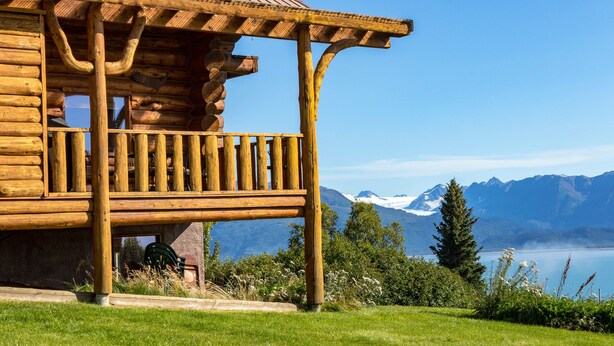 Una cabaña de madera con balcón que da a un lago y montañas.