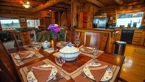 Comedor de madera con una mesa grande dispuesta para cuatro, cocina al fondo y vistas al exterior.