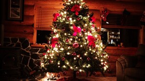 Acogedor interior de cabaña de troncos con un árbol de Navidad decorado, chimenea de piedra y paredes de madera.
