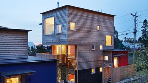 A modern multi-story house with a wooden exterior, a visible staircase, and a small outdoor seating area. - The Horizon- Award Winning- Sauna Available for a fee (Grand Marais)