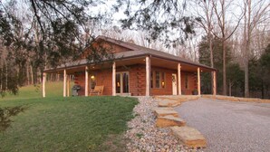 A log cabin with a porch, a grill, and a bench.