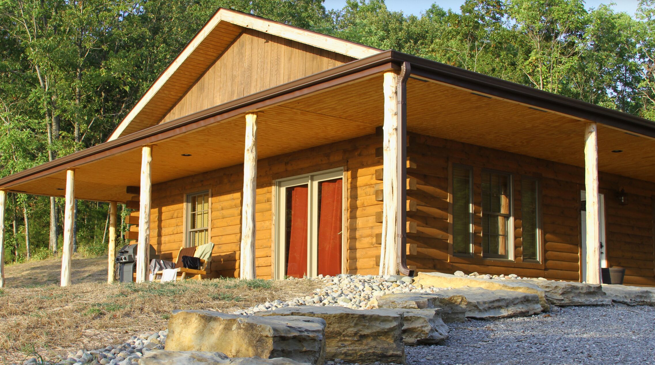A log cabin with a covered porch, large windows, and a stone foundation.