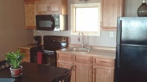A kitchen with wooden cabinets, a black refrigerator, a stove, a microwave, and a sink.